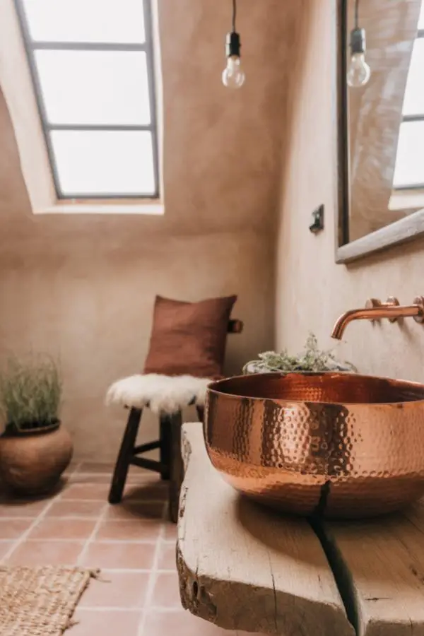 Hammered copper vessel sink from rustic bathroom design. Natural wood vanity with terra cotta flooring creates warmth.