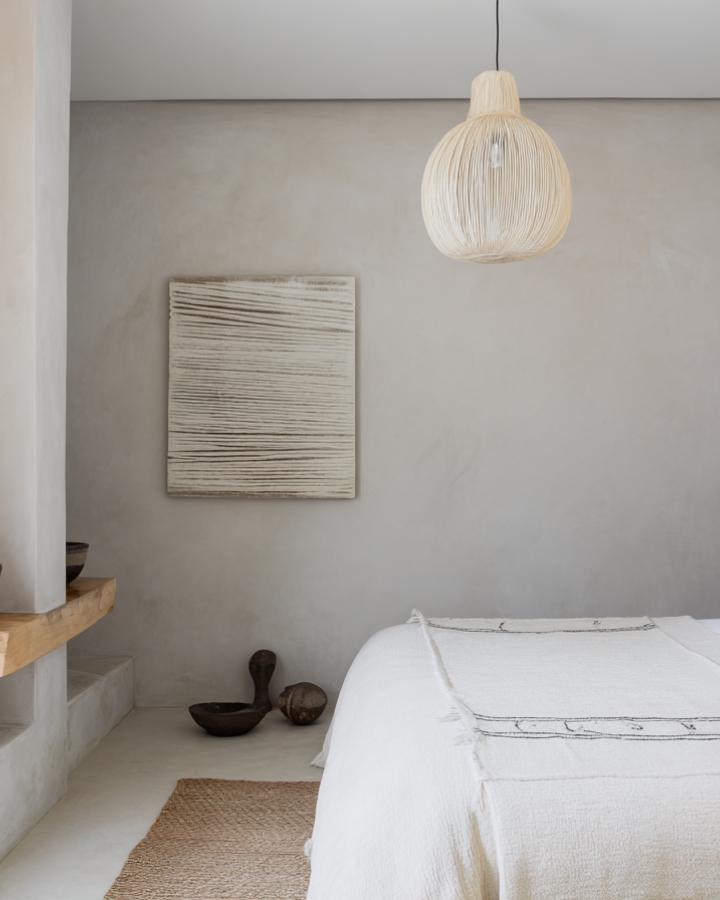 Natural woven pendant light hanging above minimalist white bedroom with textured wall art.
