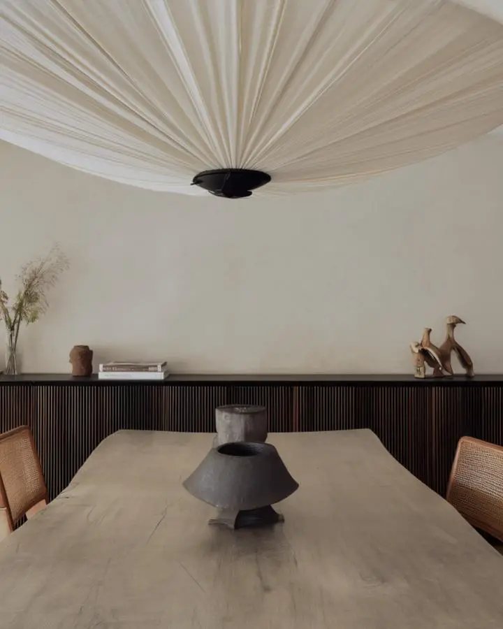 Pleated fabric ceiling fan above minimal dining table with natural wood and woven chairs.