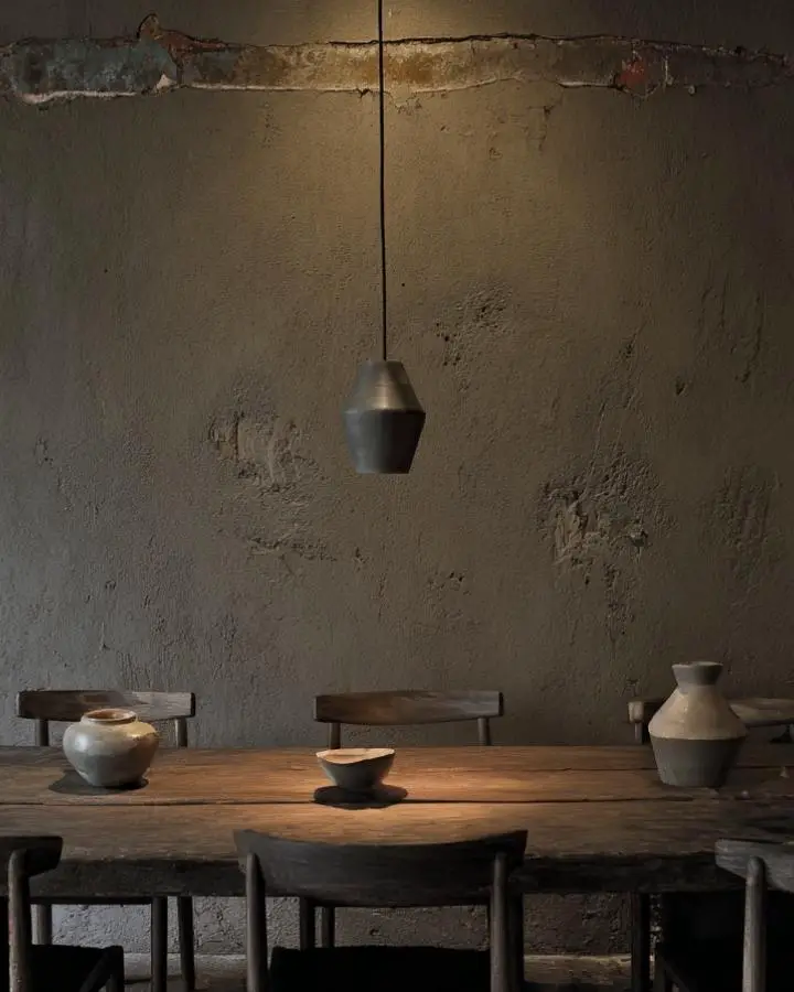 Weathered sage green wall with cracked plaster texture behind rustic wooden dining table. Distressed paint finish creates authentic aged atmosphere.