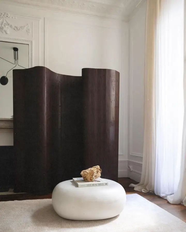 Curved walnut wood screen from @fabio__montedoro. Creates intimate seating corner with white ottoman and minimal styling.