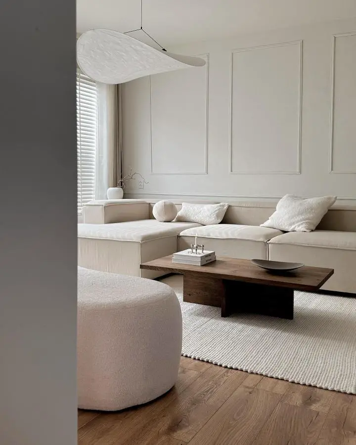 Curved white pendant light from @wonen.met.lef. Creates flowing sculptural element above neutral seating area.