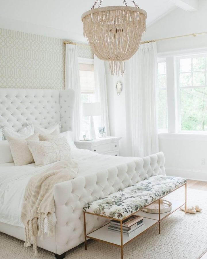 White tufted bed with floral cushioned bench from @gillaleighhome.designs showcases elegant white aesthetic bedroom ideas with cozy textures and soft natural light.