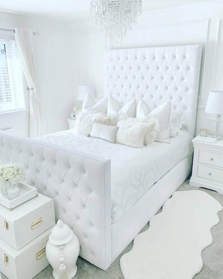 White tufted bed frame and soft accents from @stylemepretty. Bright, elegant all-white bedroom design with plush textures and crystal chandelier.