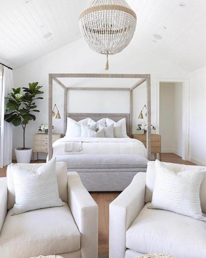 White natural fiber canopy bed and warm wood nightstands in serene bedroom by @wheretheguysreside. Plush seating and soft lighting complete the look.