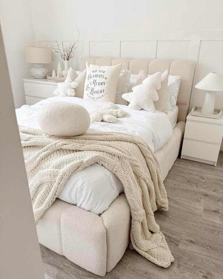 Creamy chunky knit throw on upholstered bed with textured pillows and neutral decor from @crosslettings. Soft, inviting, and minimal white bedroom style.