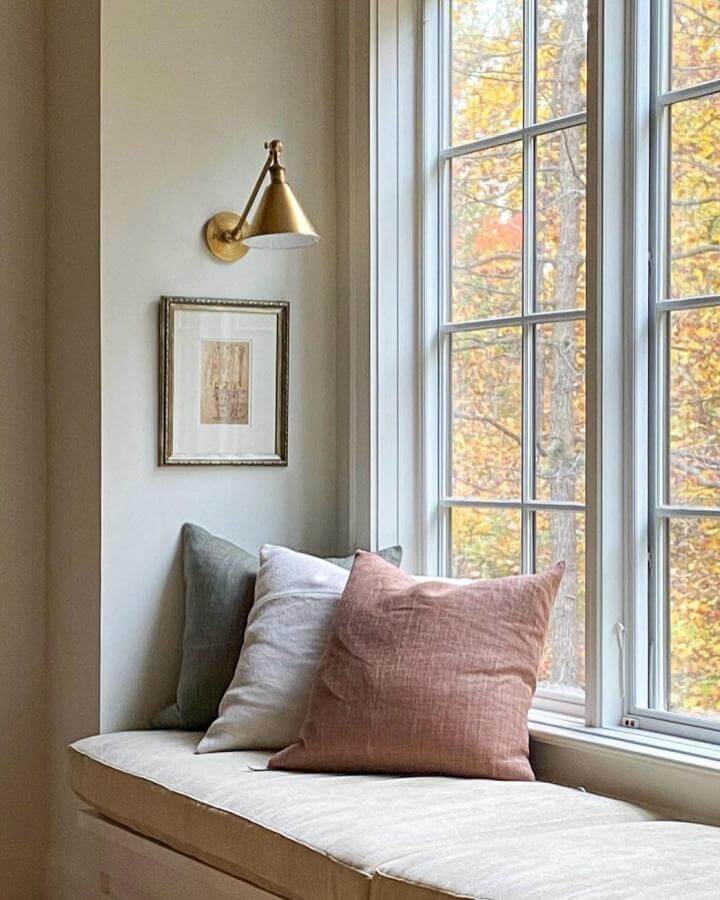Blush pink and soft gray linen pillows on a creamy window bench seat by @mollysmithwatson with autumn trees outside.