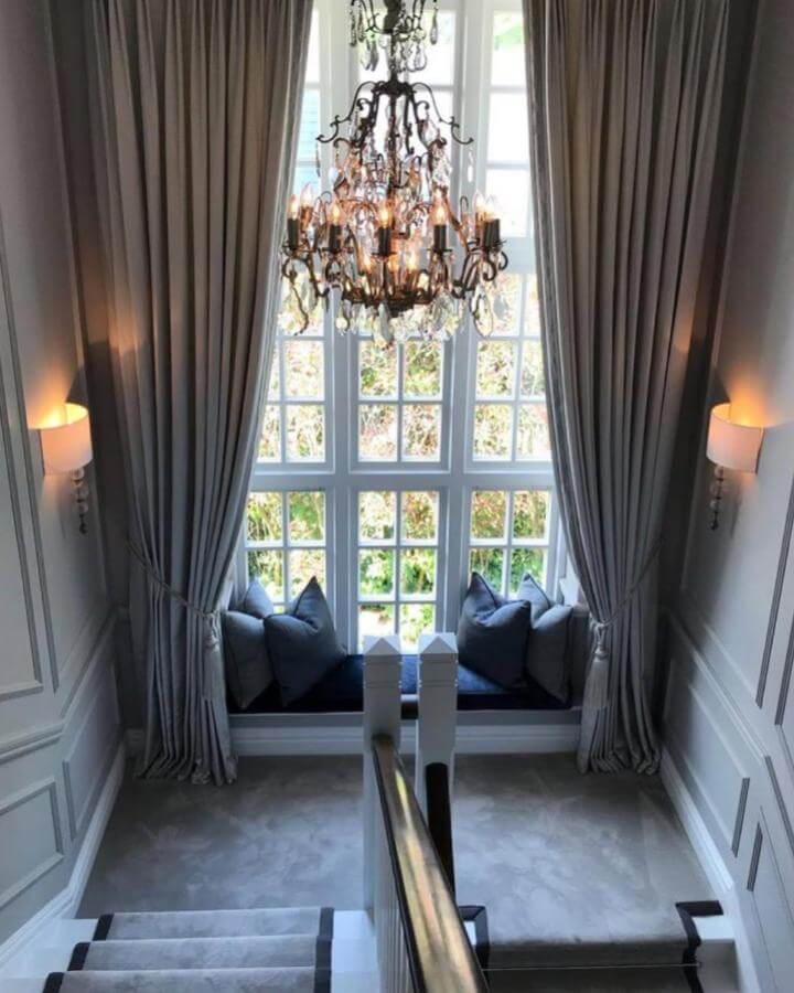 Navy velvet cushioned window seat ideas from @april_hamilton_designs with gray walls and heavy drapes in elegant stairwell nook.