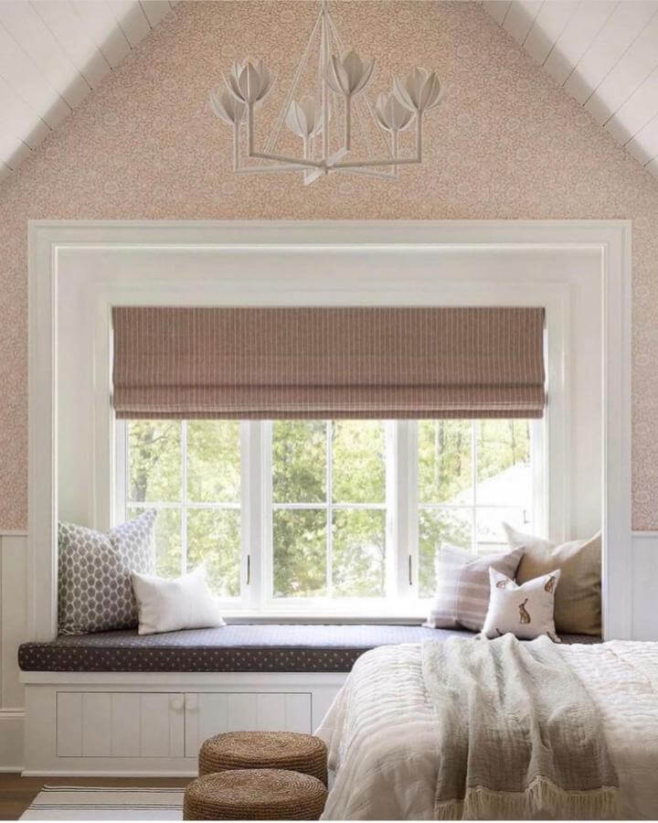 Light neutral-toned window nook with soft cushions and a woven roman shade from @jennverrierphoto in a cozy bedroom setting.