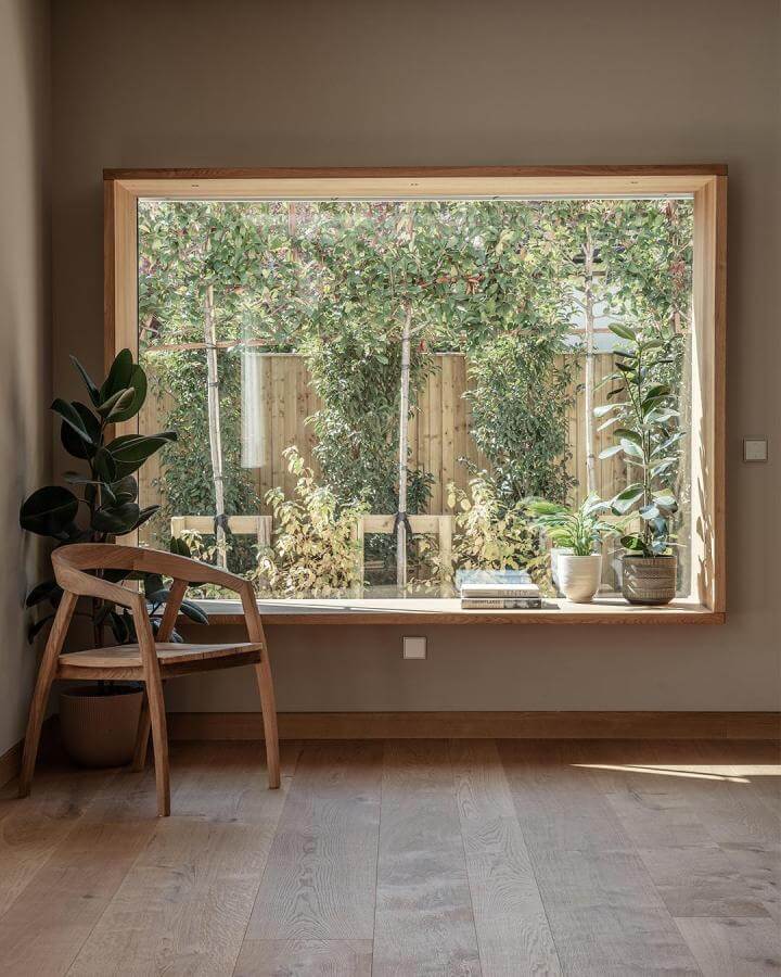 Light wood framed window seat nook from @baufritz_uk with plants and natural sunlight creating a warm inviting space.