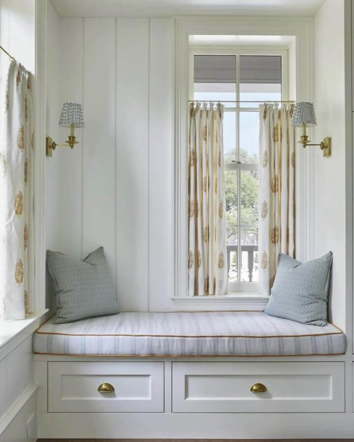 Cream and pale blue window nook with brass handles and patterned curtains from @flemingpeters featuring cushioned seating and built-in storage below.
