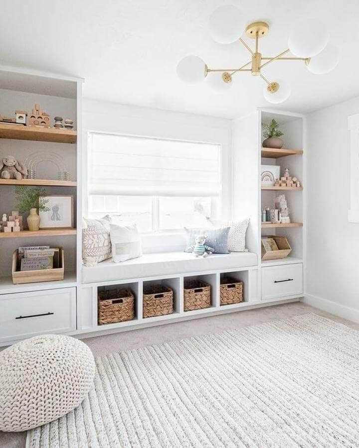Natural white built-in bench with woven baskets and soft textiles from @odonnellshome. Light-filled cozy nook with wood shelves and knit pouf.