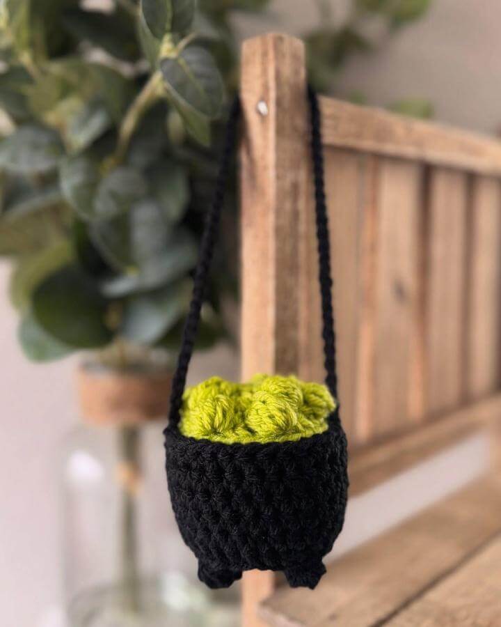 Black knitted cauldron planter from @applerose.knits. Lime green yarn filling mimics bubbling potion contents.