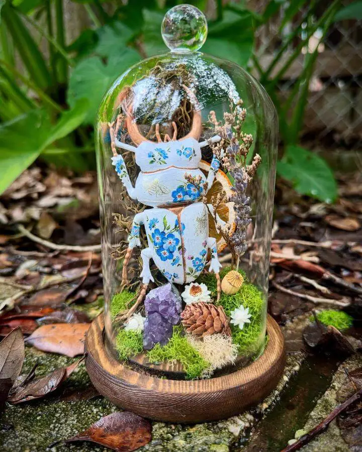 Glass terrarium display with pressed flowers and crystals from @sweetbonniebrownart featuring witchy craft ideas and natural elements.