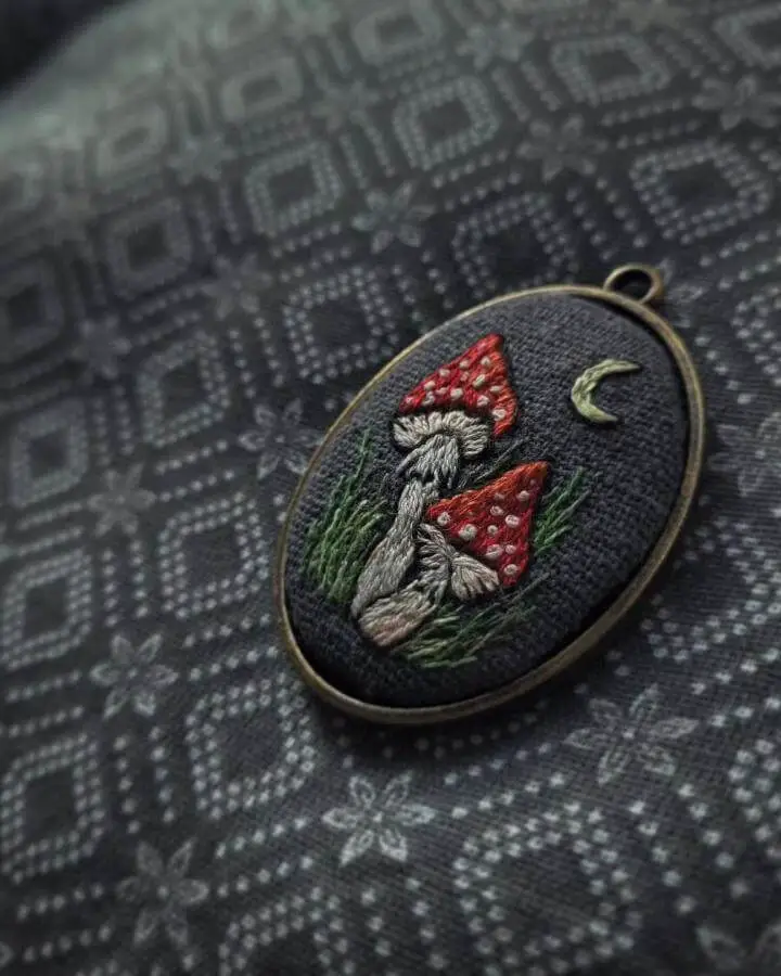 Dark embroidered pendant from @alqua_silme showcasing red mushrooms and moon for witchy craft ideas inspiration.