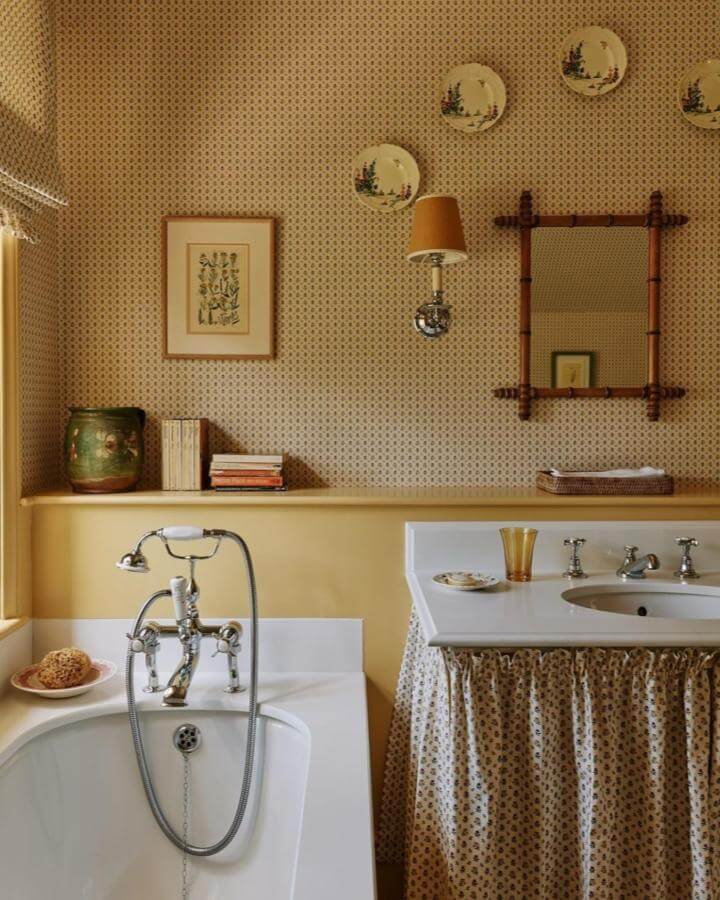 Yellow vintage bathroom decor with patterned wallpaper, fabric sink skirt, and classic chrome fixtures from @horwoodphoto. Warm and inviting space.