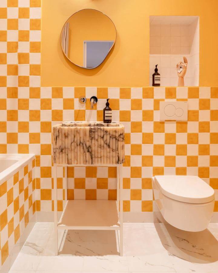 Yellow and white checkerboard tiled bathroom with marble sink and warm yellow walls from @giuliamaretti_studio bright yellow bathroom ideas with playful and elegant touches