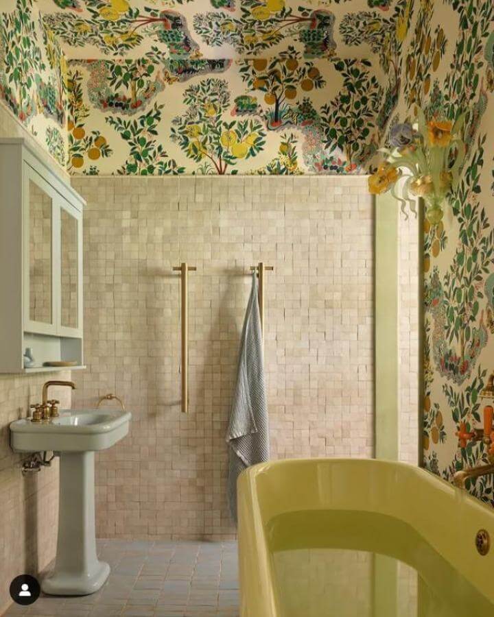 Yellow clawfoot tub and floral wallpaper bathroom from @smartanson with brass fixtures and beige tile backdrop creating yellow bathroom ideas.