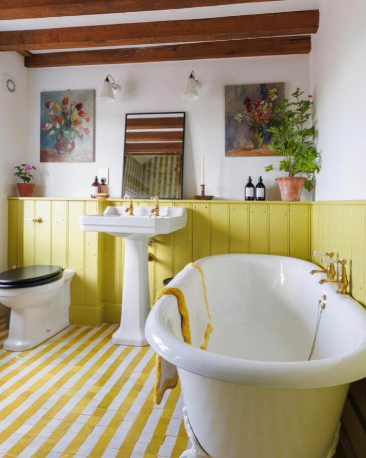 yellow wainscoting and striped floor tiles in a cozy bathroom from @juliatomsphotography featuring vintage fixtures and plants