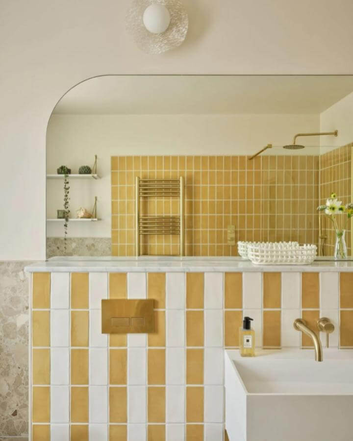 Yellow and white ceramic tiles with gold fixtures in a bathroom from @snookphotograph showing warm yellow bathroom ideas. Bright and cozy space.