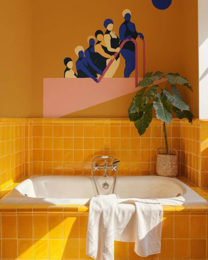 Yellow glossy square tiled bathroom with white tub and leafy plant from @coordonne featuring vibrant yellow bathroom ideas and modern wall art.