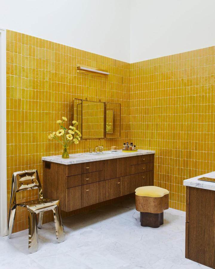 Glossy mustard yellow tile walls, wooden cabinetry, and yellow cushioned stool in bathroom from @richardpowersphoto vibrant yellow bathroom ideas bright and inviting.